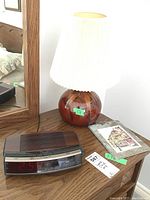 Ceramic base lamp with pleated shade, alarm clock radio, and small picture on slate on wooden surface