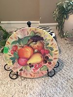 Front view of the Limoges plate showing the detailed fruit design on a metal stand.