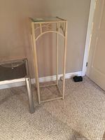 Straight angled view of tall metal frame plant stand with glass top, showing detail of frame decoration and clear glass surface.