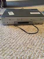 Front view of the Sony DVD player showing the disc tray, control buttons, and power button on a carpeted floor.