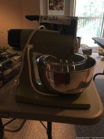 Full green Sunbeam stand mixer with stainless steel bowl attached, viewed from the side on a folding table indoors.