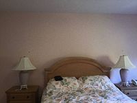 Two ceramic table lamps on bedside tables on each side of a bed with floral bedding, against a beige wall.