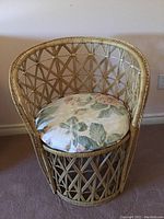 Front and top angle view of the round wicker chair with floral round cushion on carpeted floor against plain wall.