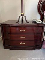 Front view of one dark wood night table showing 3 drawers and brass handles.