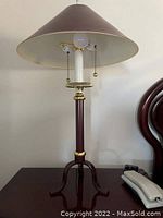 Photo showing one of two matching table lamps with burgundy conical shade, gold trim, and tripod wooden base.