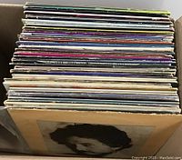 Box of over 50 vinyl records showing album spines and covers, packed closely together.