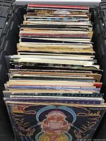 Crate of stacked vinyl LP records viewed from front, showing various album spines and covers