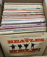 Top view of cardboard box filled with over 100 empty record covers showing The Beatles 'Help!' cover on top with visible aging and wear.