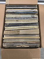 Full box shot of over 50 vinyl records stacked vertically with visible wear and aging on album covers.
