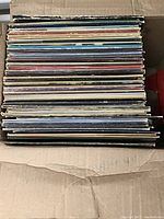 Box containing over 50 vinyl records stacked vertically showing various album spines.