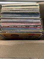 Box containing over 40 vinyl records stacked vertically showing the edges and spines of various album covers.