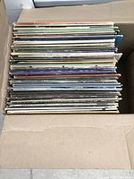 Box of over 40 vinyl records stacked vertically, showing various album cover edges and spines.