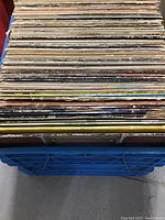 Side view of a large stack of vinyl records in sleeves showing wear and aging.
