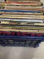 Photo of over 40 vinyl records stored upright in a blue plastic crate showing varied album spines and covers.