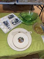 Wide view showing green glass bowls, white ceramic dessert set with gold trim and scenic designs, small pinkish glass bowl, and white ceramic divided tray with blue scenic designs on green tablecloth.