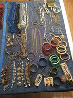 Full overview of assorted costume jewelry laid out on blue fabric, showing necklaces, bracelets, bangles, pins, rings and other items.