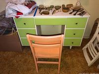 Front view of Mid Century Modern desk with green drawers and pink wood chair placed in front.