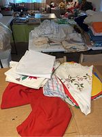 Pile of assorted linen pieces including embroidered napkins, doilies, handkerchiefs, red cloths, and small table coverings