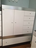 Front view of the dresser showing the white drawer fronts and cabinet doors with brushed metal trim and small round knobs.