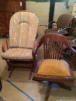 Two vintage wooden chairs, one a swivel office chair with gold seat cushion, the other a wood framed glider with tufted beige upholstery.