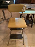 Front view of yellow vinyl covered kitchen stool with seat and backrest.