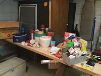 Wide view showing Mustang yellow insulated ice chest, various colorful Thermos containers, two oil lanterns, soft cooler bag, cleaning supplies in boxes, wooden clothespins, and metal tins labeled Band Aid.