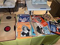 Overview of various vintage music sheets and records on a table showcasing colorful covers including Judy Garland and Paul Whiteman.