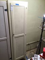 Front view of tall white wooden pantry cabinet with single door and metal knob.