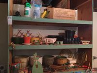 Shelves filled with multiple ceramic and plastic garden planters of different sizes, shapes, and colors along with garden hand tools and rolling plant stands.