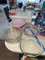 Photo showing multiple clear glass Pyrex casserole dishes with lids and a distinctive pink Pyrex mixing bowl among other kitchen items.