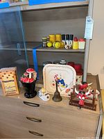 Overview of items on wooden dresser: salt and pepper shakers, novelty mushroom toothpick holders, vintage bell, napkin corral with cow figures, and onion tape dispenser