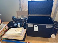 Overall lot shows sewing machine, open carrying case, manuals and accessories on table