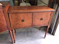 Front view of vintage True Grand Rapids wooden cabinet showing two doors and carved legs.