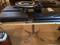 Three vintage turntables displayed side by side on a table: McDonald 500A on left, JVC AL-A151 on right, Sansui Lineair P-M50 top center with open tonearm.