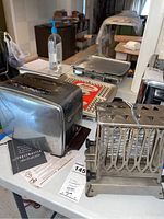 Vintage chrome Toastmaster toaster with original instruction manual placed next to Sunbeam waffle baker/grill on table.
