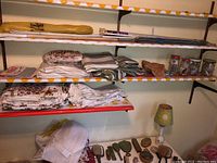 Shelves with packaged curtain rods, folded vintage curtains with floral and striped designs, jars with hooks and hardware, and lampshade.