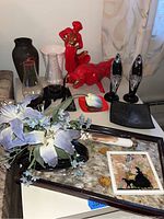 Photo shows red ceramic bullfighter figurine and bull figurine with gold painted accents, nearby glass hurricane candle holders and vases, plus black sunburst patterned plate.