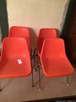 Front view of four orange mid century plastic chairs with metal bases.