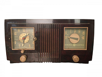 Front view of General Electric vintage tube radio featuring clock and radio tuner dials with knobs and grille.