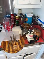 Overview of vintage kitchenware including pitchers, teapots, metal coffee decanters, ceramic items, a food chopper, nutcrackers, and a cutting board with tools.