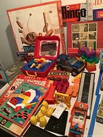 Wide view of lot showing multiple vintage board games, toy tools, toy cars, puzzles, and wooden stacking toy.