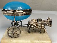 Side view of silver donkey pulling domed blue glass carriage on marble base