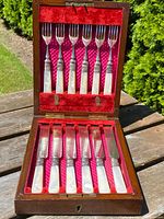 Full open view of set showing six fish forks with mother of pearl handles and sterling silver collars mounted in upper section of velvet-lined solid oak box.