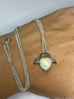 Pendant necklace on wrist showing heart-shaped opal with silver wings and silver chain.
