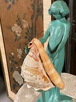 Side view of the lamp showing the green patinated metal figural nude holding the carved conch shell shade with cameo scenes on square base.