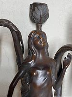 Close-up of female figure bust and upper arms showing leaf-form candle holder