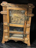 Front angled view of the Arts & Crafts era solid oak table clock showing face, wooden slat design, and brass hardware.