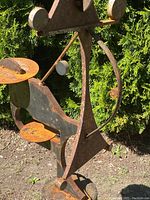 Mid-section close-up showing rusted iron triangular plate and suspended circular disc