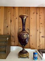 Full frontal view of the vase on a white surface with soda can for scale against wood-panel background.