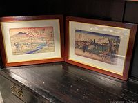 Two framed Japanese woodblock prints side by side on a dark surface
